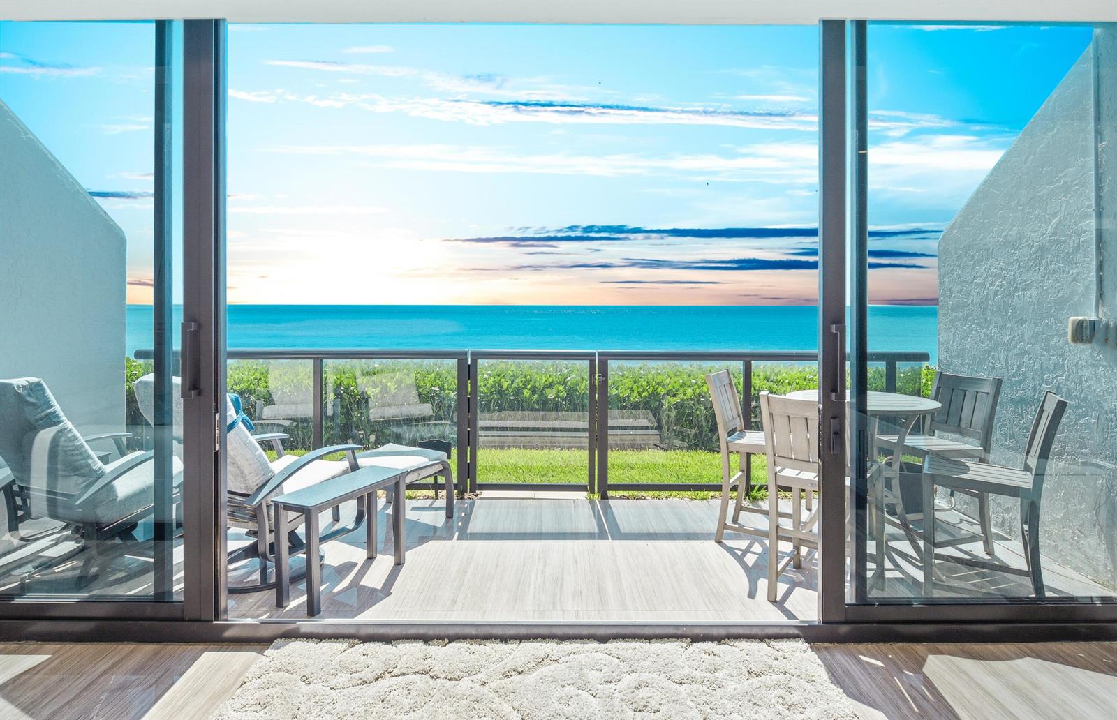 A patio with outdoor furniture overlooks a grassy lawn and the ocean through sliding doors — 3115 S Ocean Boulevard # 103, Highland Beach FL 33487, HIGHLAND BEACH, FL