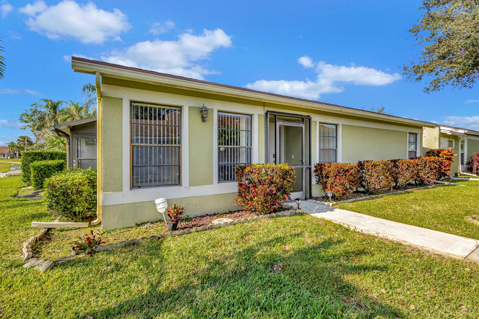 A single-story house with light green stucco walls, a screened front door, and landscaped bushes — 4385 Willow Brook Circle, West Palm Beach FL 33417, WEST PALM BEACH, FL