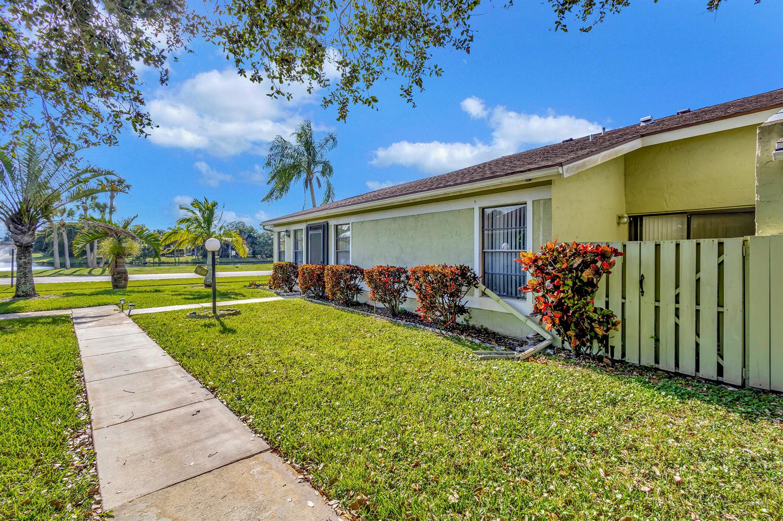 A light green single-story house exterior with a sidewalk, lawn, and a wooden privacy fence — 4385 Willow Brook Circle, West Palm Beach FL 33417, WEST PALM BEACH, FL