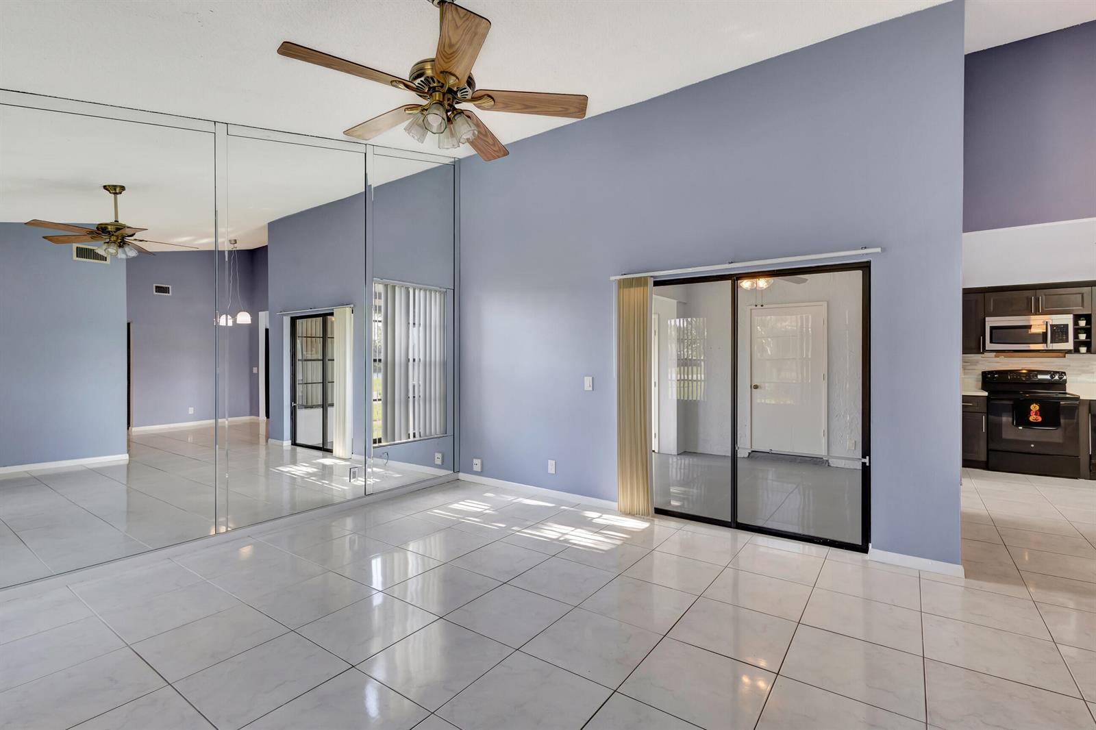 A living room with light blue walls, white tile flooring, a mirrored wall, and a ceiling fan — 4385 Willow Brook Circle, West Palm Beach FL 33417, WEST PALM BEACH, FL