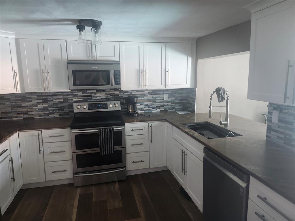 A kitchen features white cabinets, dark countertops, stainless steel appliances, and a tiled backsplash — 8501 HUNTING SADDLE DRIVE, HUDSON, FL