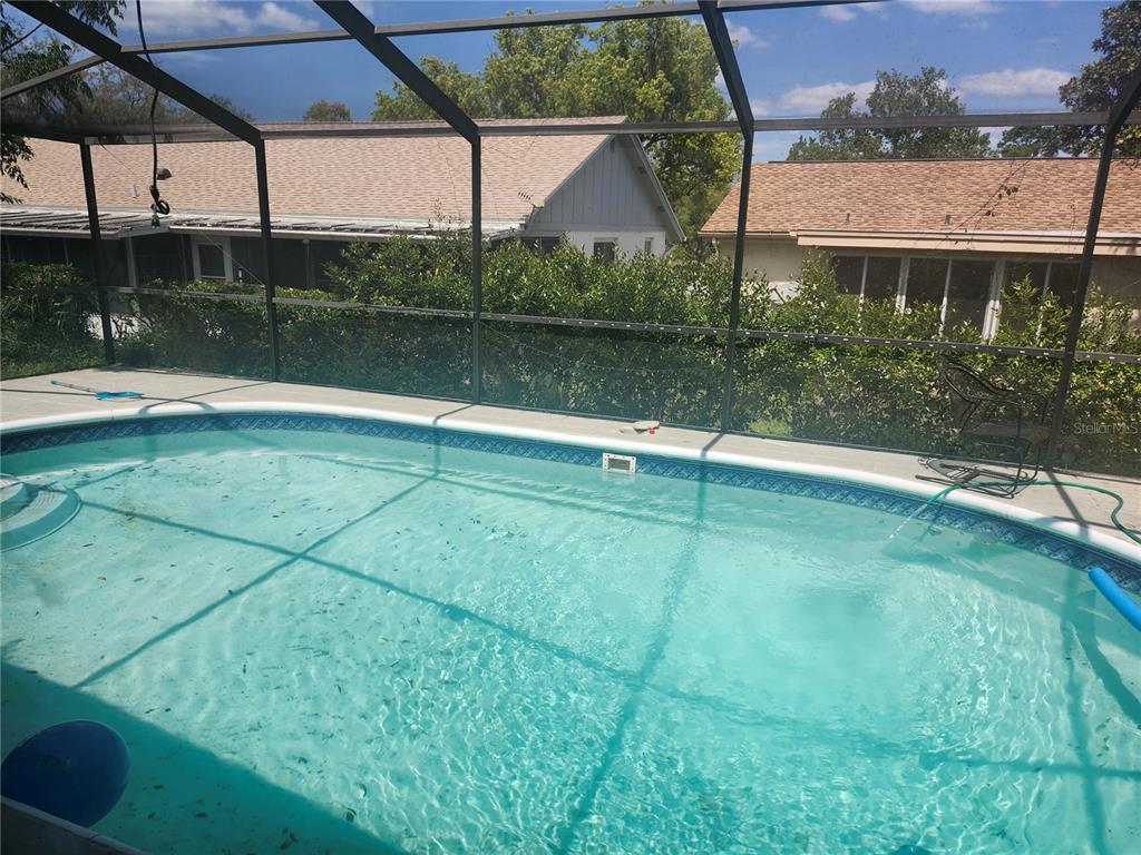 A swimming pool enclosed by a screened-in lanai with neighboring houses visible in the background — 8501 HUNTING SADDLE DRIVE, HUDSON, FL