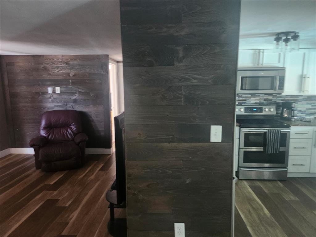 A view of a living area and kitchen featuring dark wood-paneled walls and flooring — 8501 HUNTING SADDLE DRIVE, HUDSON, FL