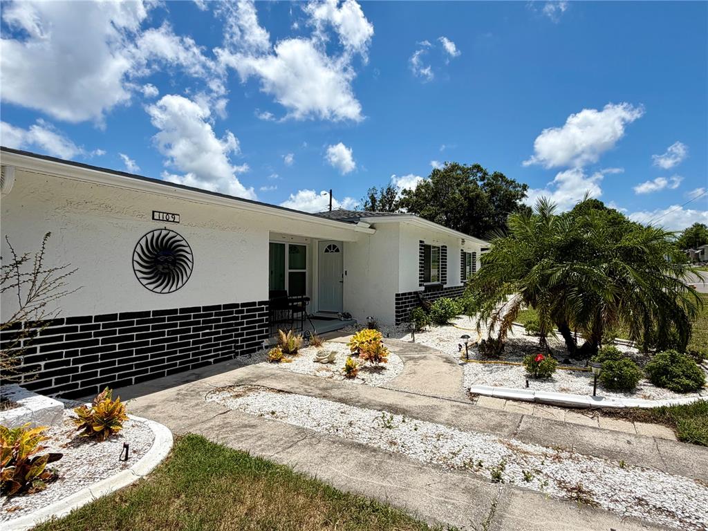 A white house with a black brick base, a sun wall decoration, and a palm tree — 1109 S BETTY LANE, CLEARWATER, FL
