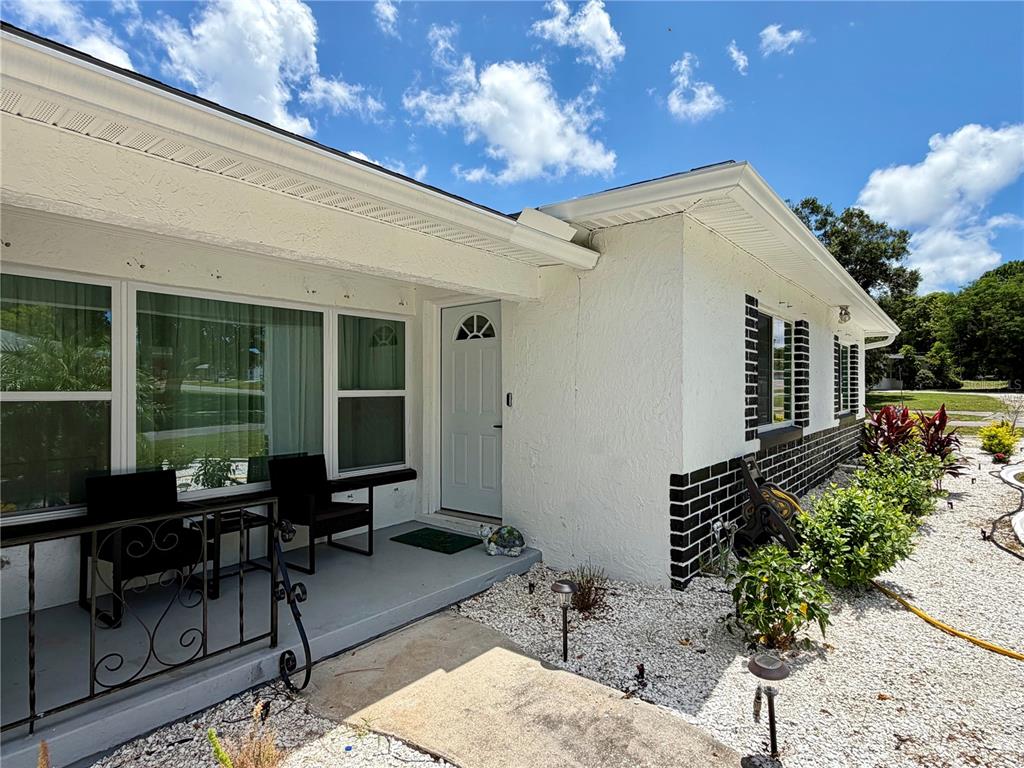 A white stucco house exterior features a front porch, a white door, and black brick accents — 1109 S BETTY LANE, CLEARWATER, FL