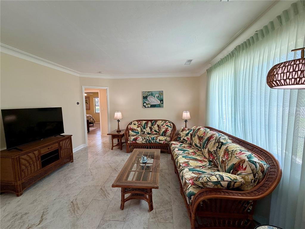 A living room features tropical-print rattan furniture, a glass-top coffee table, and light tile flooring — 1109 S BETTY LANE, CLEARWATER, FL
