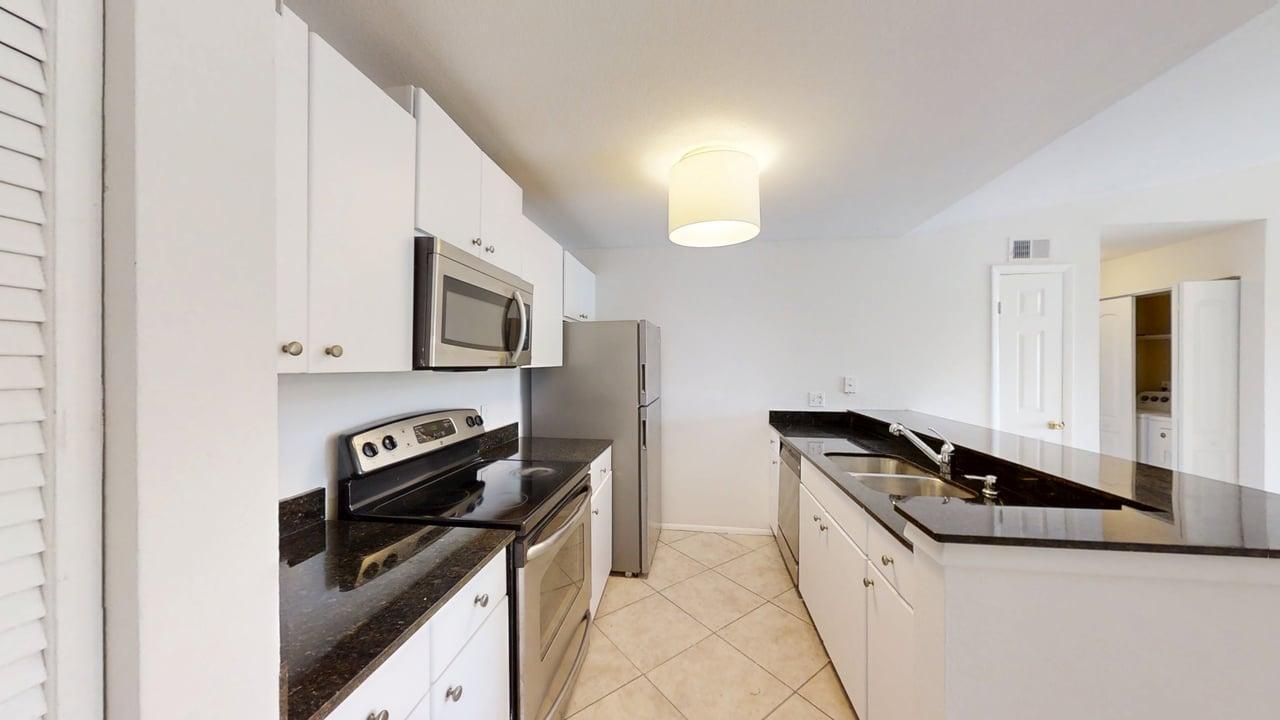A kitchen features white cabinets, dark granite countertops, stainless steel appliances, and tile flooring — 1885 Palm Cove Boulevard # 307, Delray Beach FL 33445, DELRAY BEACH, FL