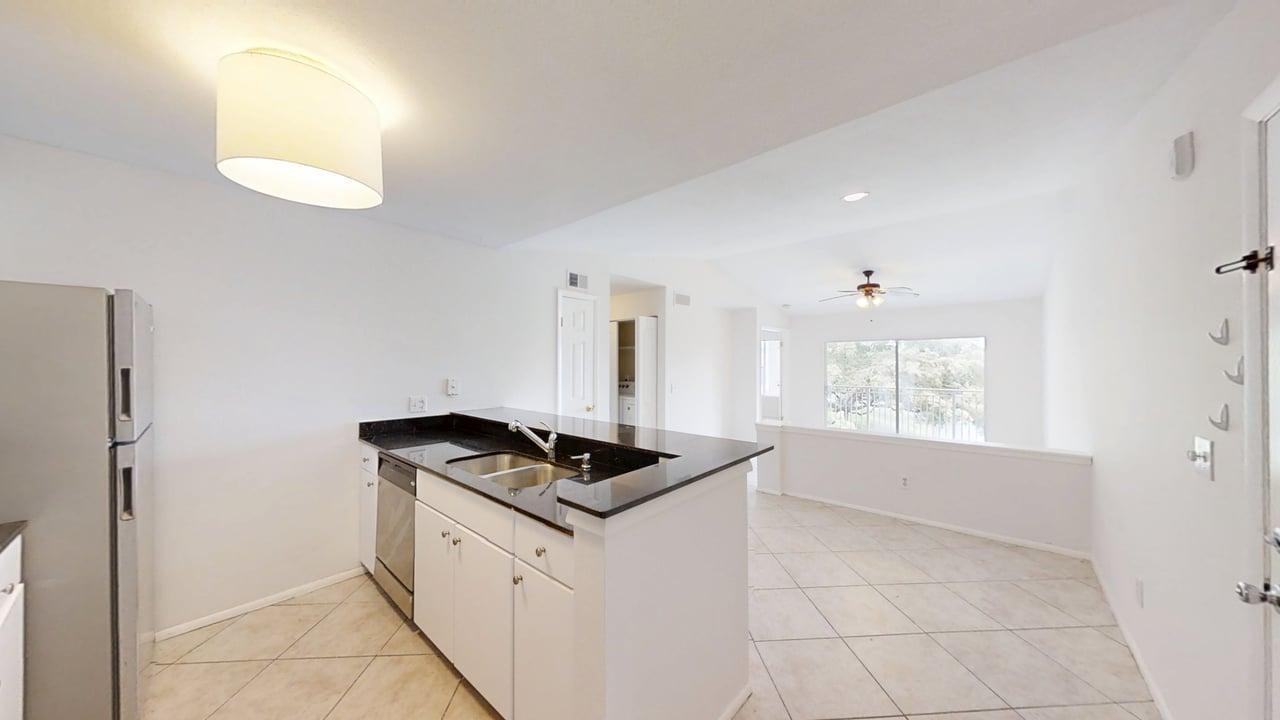 A kitchen with white cabinets and black countertops overlooks a living area with tile floors — 1885 Palm Cove Boulevard # 307, Delray Beach FL 33445, DELRAY BEACH, FL