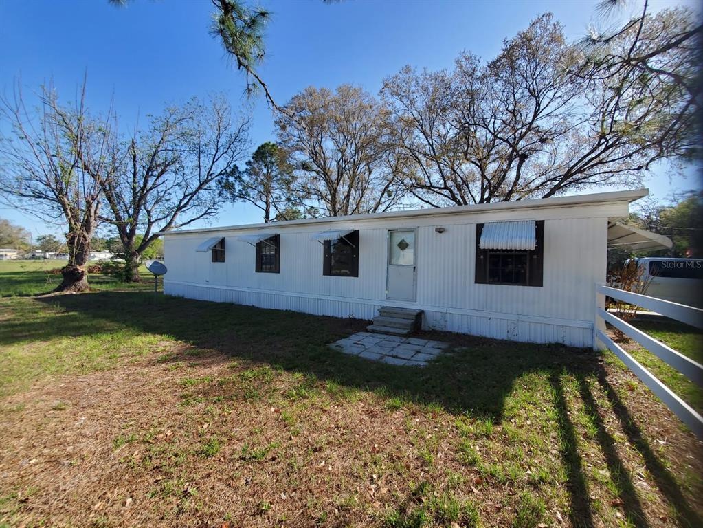 A white mobile home with brown shutters sits on a grassy lot with large trees — 37021 PAULS DRIVE, ZEPHYRHILLS, FL