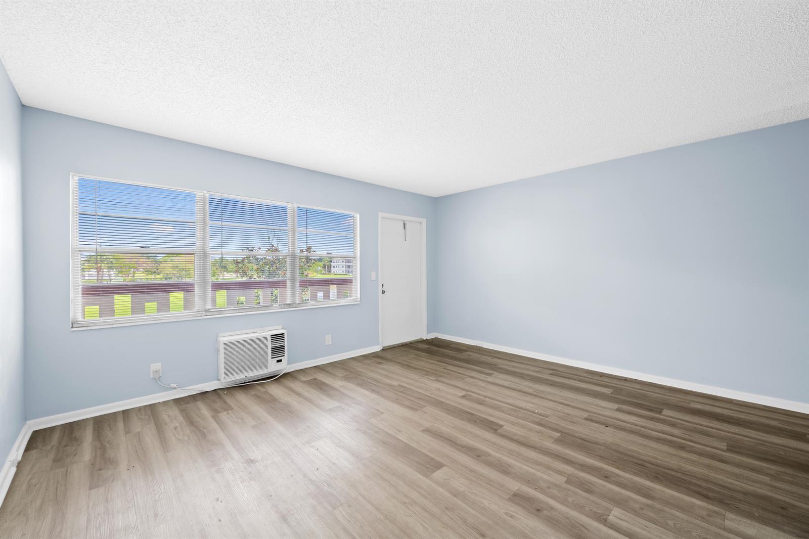 An empty room with light blue walls, wood-look flooring, a window, and a wall-mounted air conditioner — 148 Preston Way # 148, Boca Raton FL 33434, BOCA RATON, FL