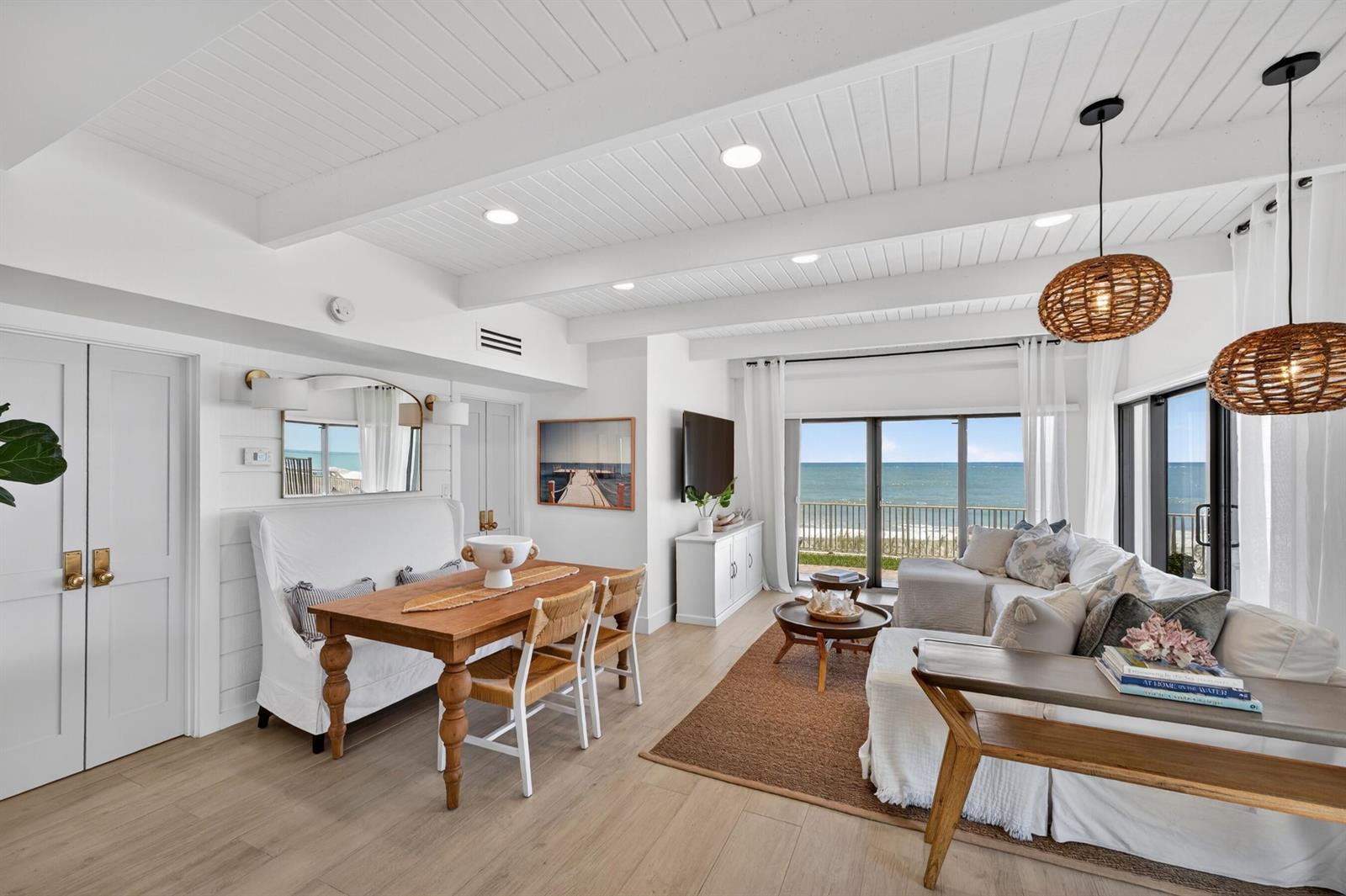 A bright, open-concept living and dining room features white shiplap ceilings, wood flooring, and ocean views — VERO BEACH, FL