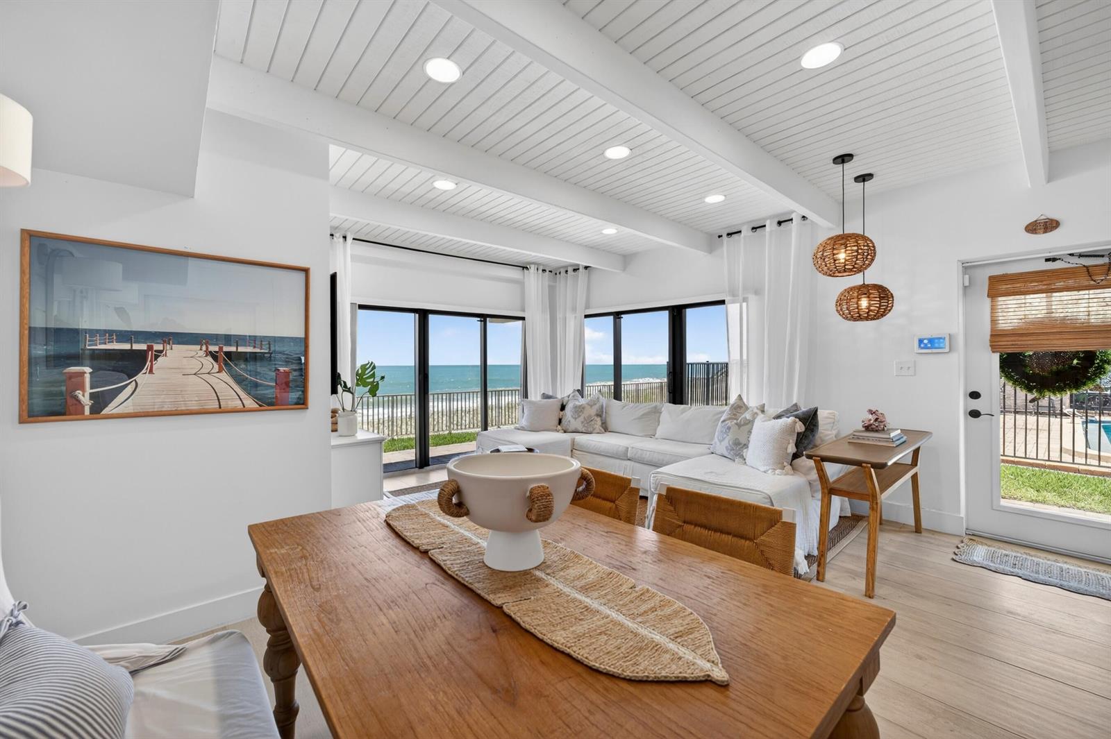 A bright living and dining area features white vaulted ceilings, wood furniture, and ocean views — VERO BEACH, FL
