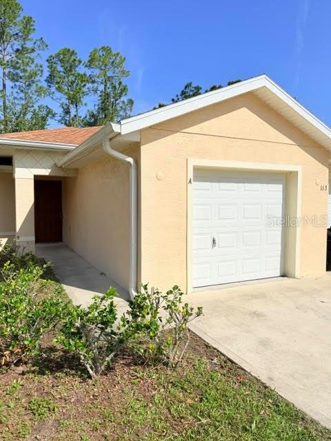 A single-story house with a tan stucco exterior, a garage, and a front entryway — 113 BRUNSWICK LANE UNIT A, PALM COAST, FL