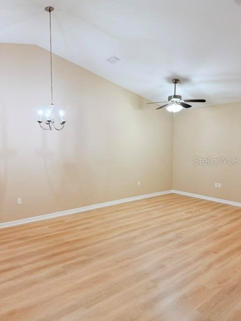An empty room with light wood-look flooring, a vaulted ceiling, a chandelier, and a fan — 113 BRUNSWICK LANE UNIT A, PALM COAST, FL