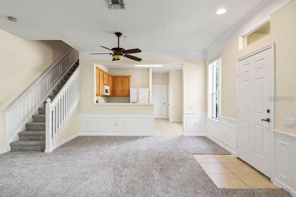 A carpeted living room features a staircase, a ceiling fan, and an open kitchen view — 6491 DAYSBROOK DRIVE UNIT 101, ORLANDO, FL