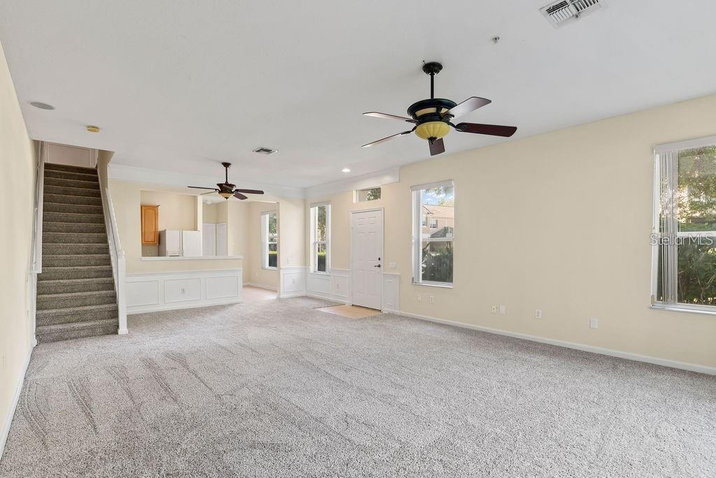 A spacious living room features beige walls, gray carpeting, two ceiling fans, and a staircase — 6491 DAYSBROOK DRIVE UNIT 101, ORLANDO, FL