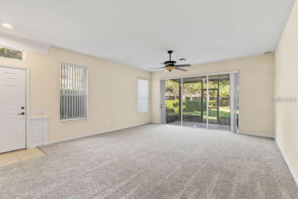 A carpeted living room features a ceiling fan, sliding glass doors, and a side door — 6491 DAYSBROOK DRIVE UNIT 101, ORLANDO, FL
