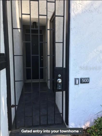 A black metal security gate leads to the front door of a white stucco townhome — 503 AVENUE B NW UNIT 503, WINTER HAVEN, FL