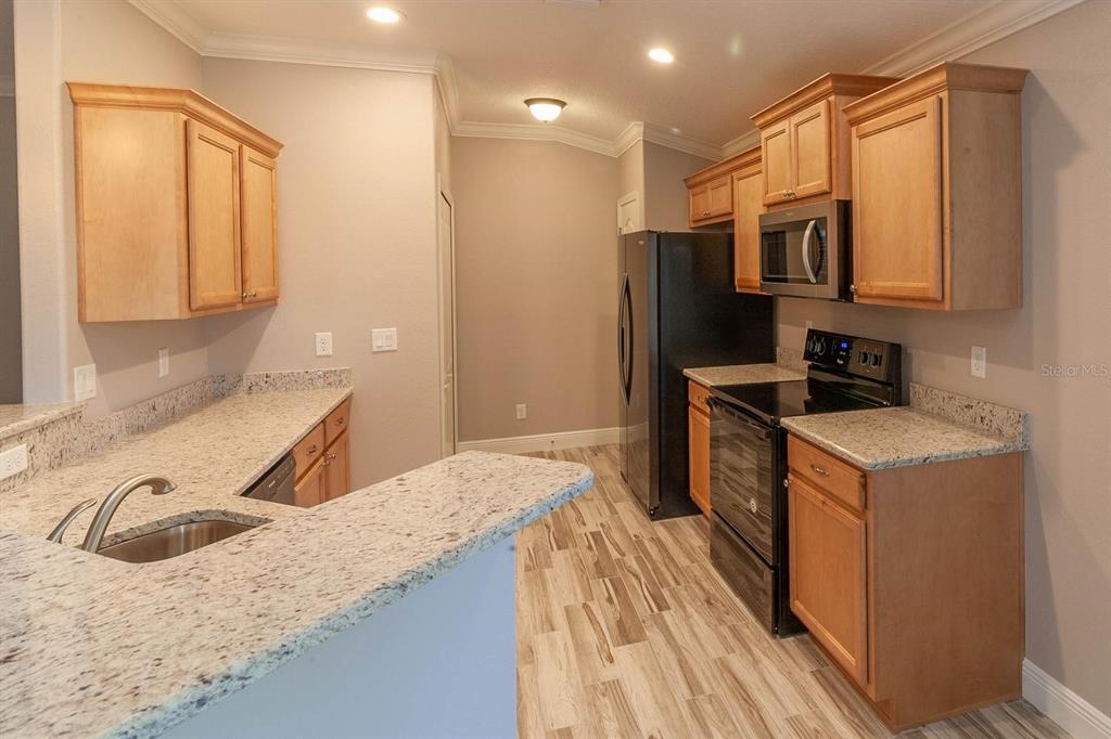 A kitchen with light wood cabinets, granite countertops, and black appliances on wood-look flooring — 16200 LENORD STREET, UMATILLA, FL