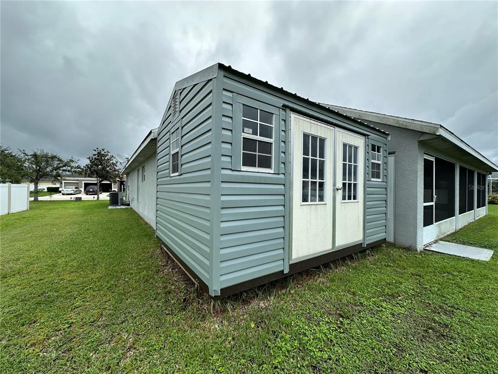 A light blue storage shed with double doors sits on a lawn beside a house — 2711 46TH STREET E, PALMETTO, FL