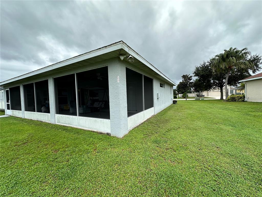 A view of a house exterior featuring a screened-in porch and a large grassy yard — 2711 46TH STREET E, PALMETTO, FL