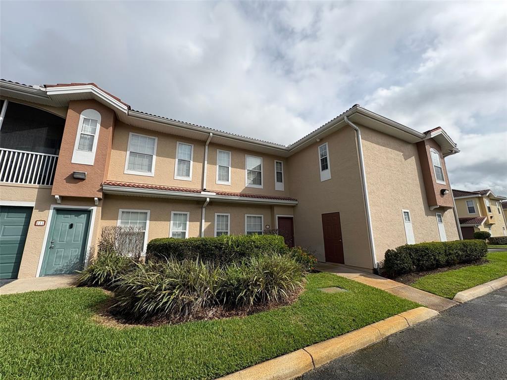 A two-story tan stucco townhouse exterior features a green front door and landscaped bushes — 12021 VILLANOVA DRIVE UNIT 112, ORLANDO, FL