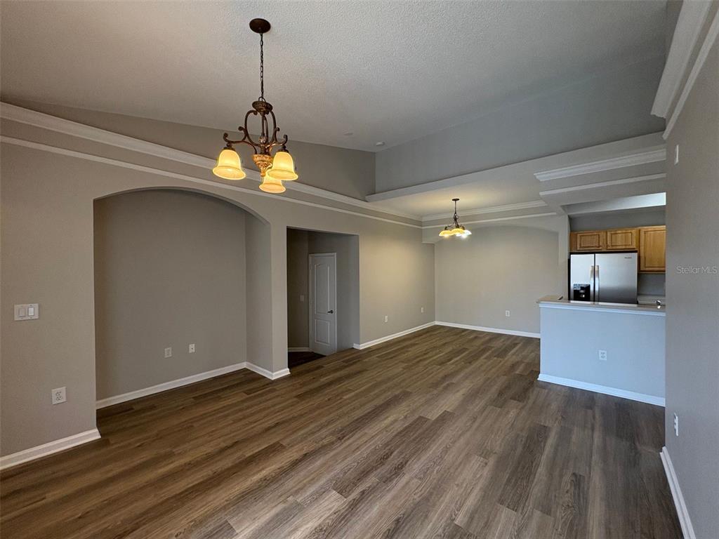 An open-concept living and dining area features wood-look flooring, vaulted ceilings, and two light fixtures — 12021 VILLANOVA DRIVE UNIT 112, ORLANDO, FL