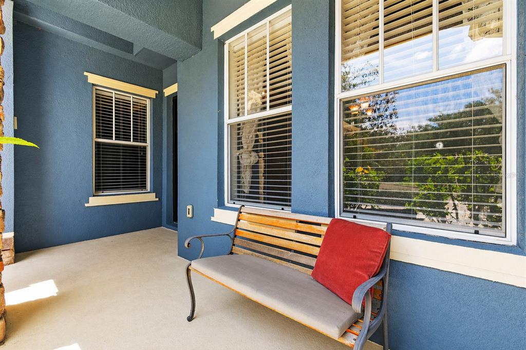 A blue-walled covered porch features a wooden bench with a red cushion and windows — 20629 WILD PLUM COURT, LAND O LAKES, FL
