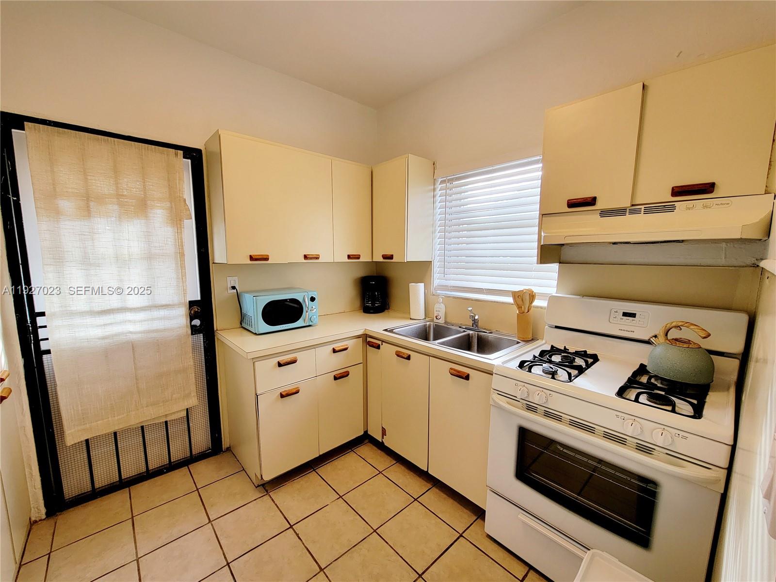 A kitchen features light-colored cabinets, a white stove, a double sink, and tile flooring — 1872 SW 9th St, Miami FL 33135, MIAMI, FL