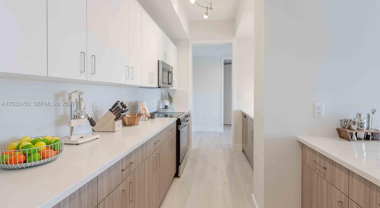A galley-style kitchen features white upper cabinets, wood-tone lower cabinets, and light-colored countertops — 151 NE 5th Ave, Delray Beach FL 33483, DELRAY BEACH, FL