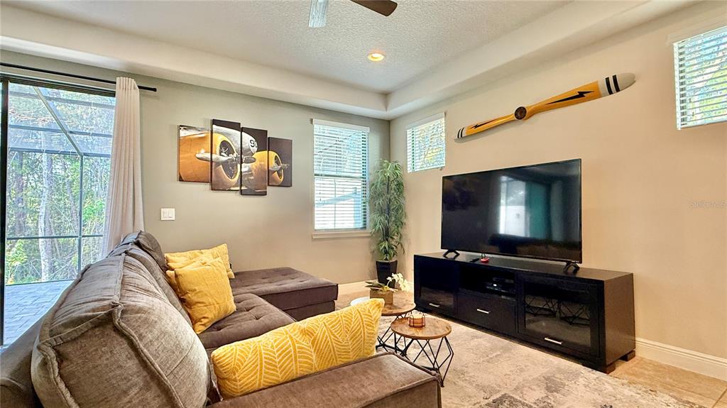 A living room features a grey sectional sofa, a television on a console, and aviation-themed decor — 8209 ROSEVILLE ROAD, DAVENPORT, FL