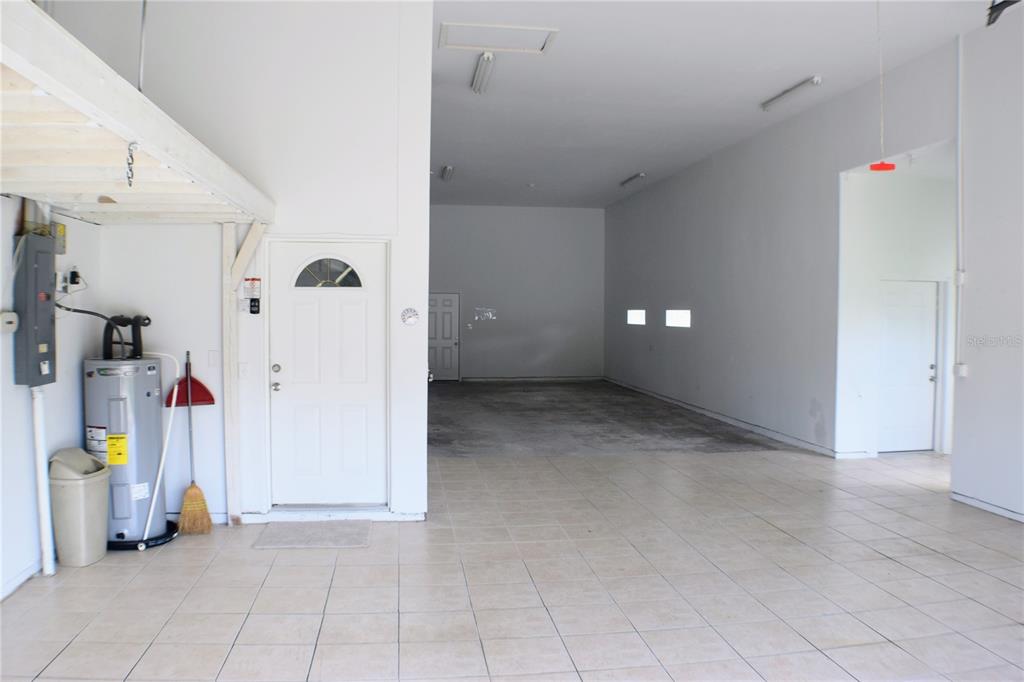 A large, tiled garage space features a water heater, white walls, and multiple doorways — 5941 MARVILLE CIRCLE, PORT ORANGE, FL