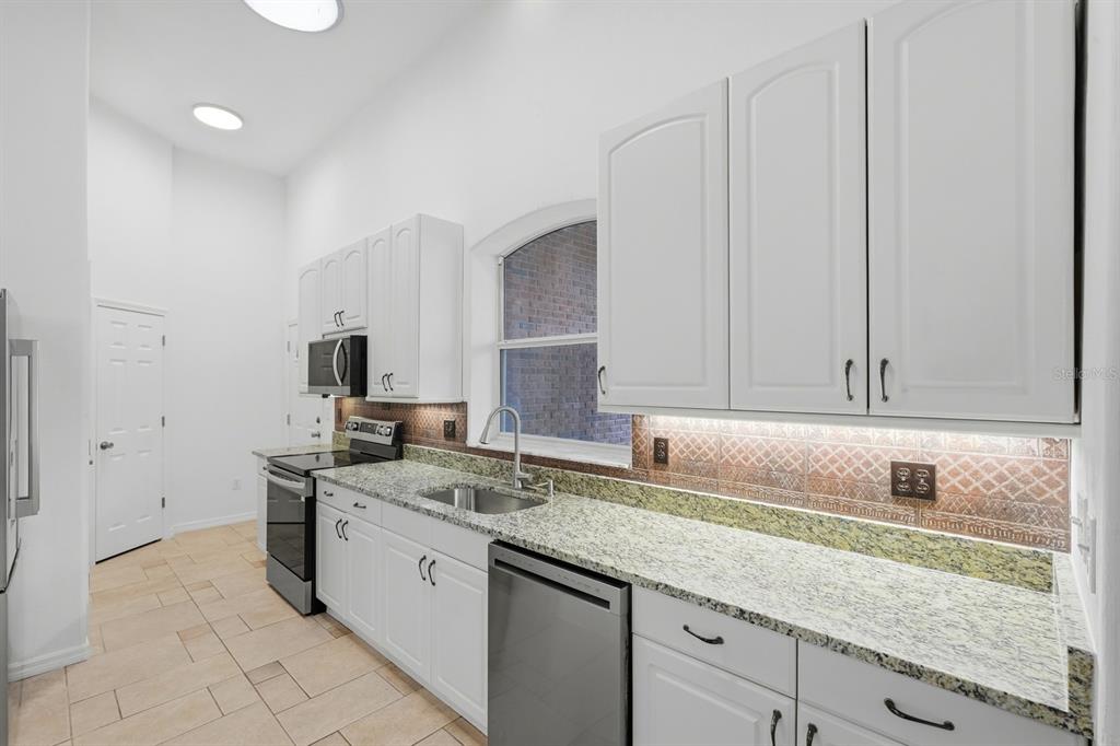 A kitchen features white cabinets, granite countertops, a stainless steel sink, and a tiled backsplash — 5941 MARVILLE CIRCLE, PORT ORANGE, FL