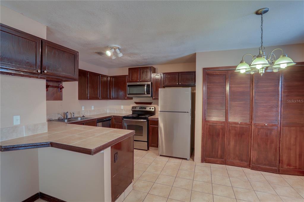 A kitchen features dark wood cabinets, stainless steel appliances, tile countertops, and a dining area — 492 TAMARACK STREET, ALTAMONTE SPRINGS, FL