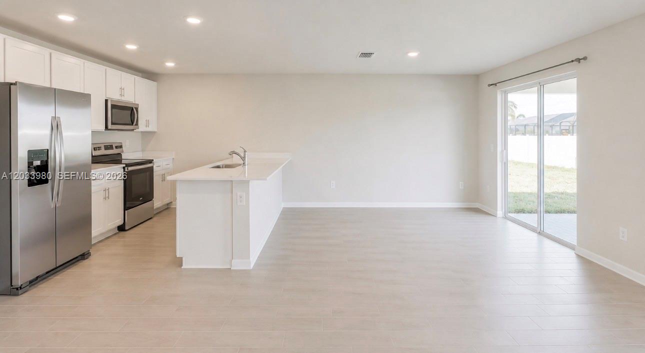 A kitchen with white cabinets, stainless steel appliances, and an island opens to a living area — 8030 OLIVE CIRCLE, La Belle FL 33935, LA BELLE, FL