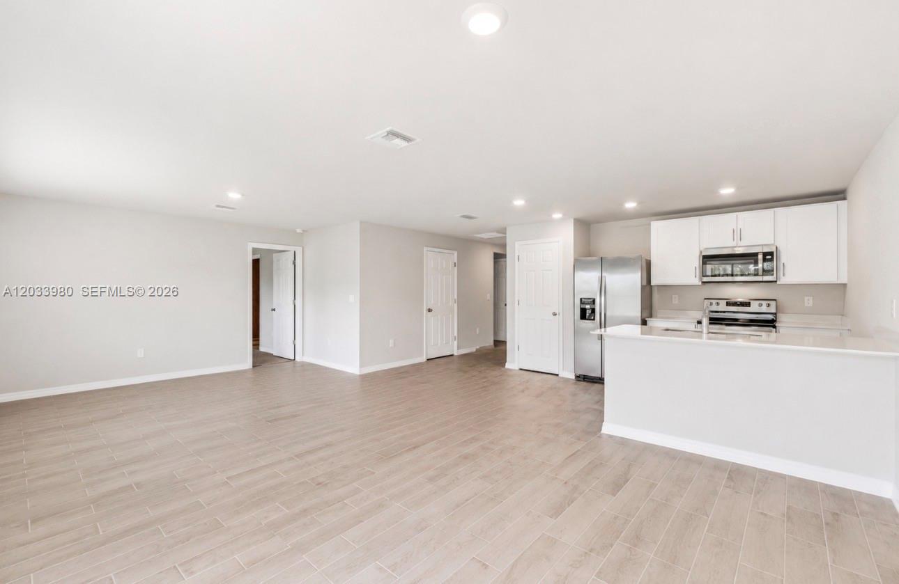 An open-concept kitchen and living area feature light wood-look tile floors and white cabinetry — 8030 OLIVE CIRCLE, La Belle FL 33935, LA BELLE, FL