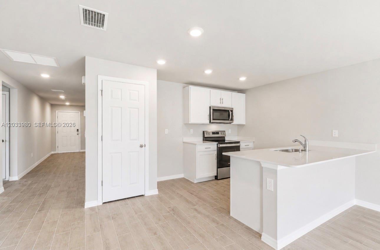 A modern kitchen features white cabinets, stainless steel appliances, and a quartz-topped island — 8030 OLIVE CIRCLE, La Belle FL 33935, LA BELLE, FL