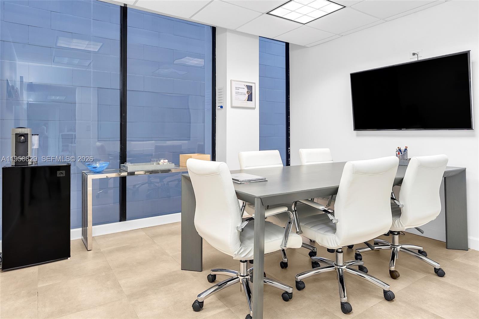 A modern conference room features a gray table, four white chairs, and a wall-mounted television — 1110 Brickell Ave # 806, Miami FL 33131, MIAMI, FL