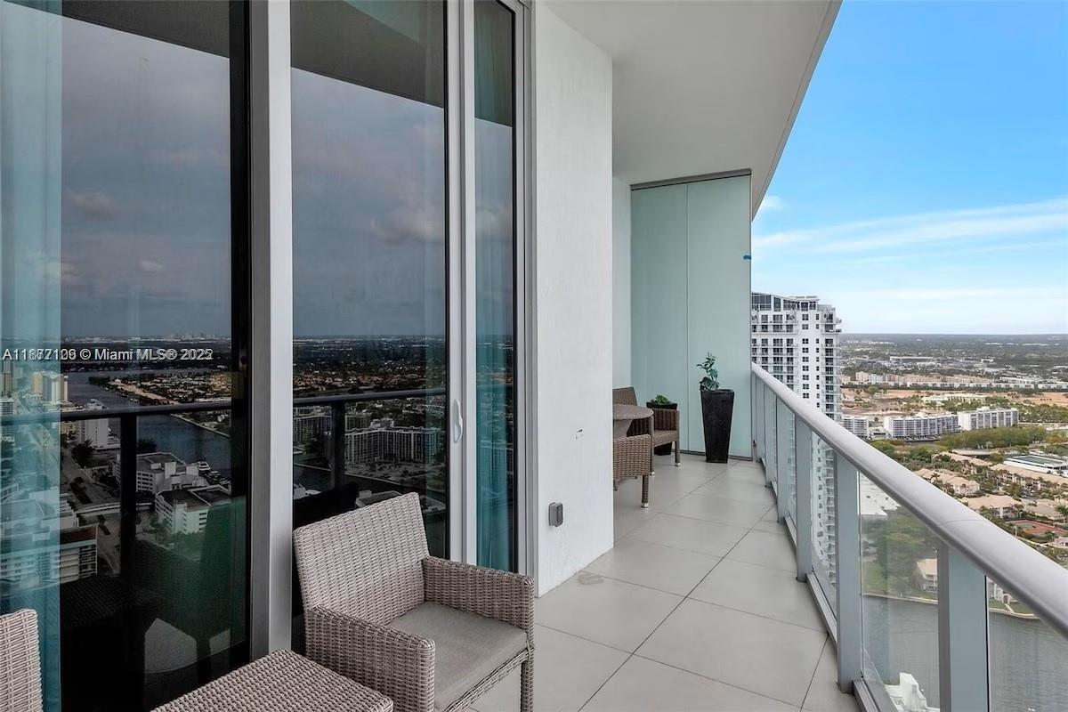 A high-rise balcony features tiled flooring, wicker furniture, and a glass railing overlooking a city — 4111 S Ocean Dr, Hollywood FL 33019, HOLLYWOOD, FL