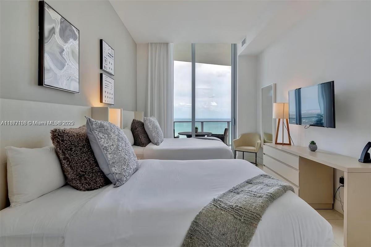 A modern hotel bedroom features two beds, a wall-mounted television, and floor-to-ceiling ocean views — 4111 S Ocean Dr, Hollywood FL 33019, HOLLYWOOD, FL
