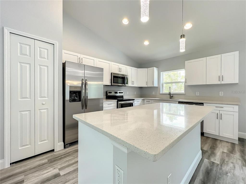 A modern kitchen features white cabinetry, stainless steel appliances, and a large quartz-topped island — 15962 SW 53RD COURT, OCALA, FL