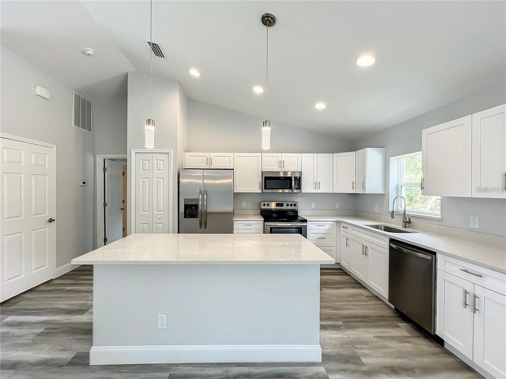 A modern kitchen features white cabinets, stainless steel appliances, a center island, and wood-look flooring — 15962 SW 53RD COURT, OCALA, FL