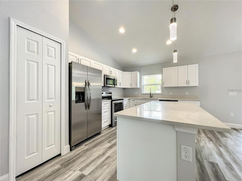 A modern kitchen features white cabinets, stainless steel appliances, a quartz island, and wood-look flooring — 15962 SW 53RD COURT, OCALA, FL