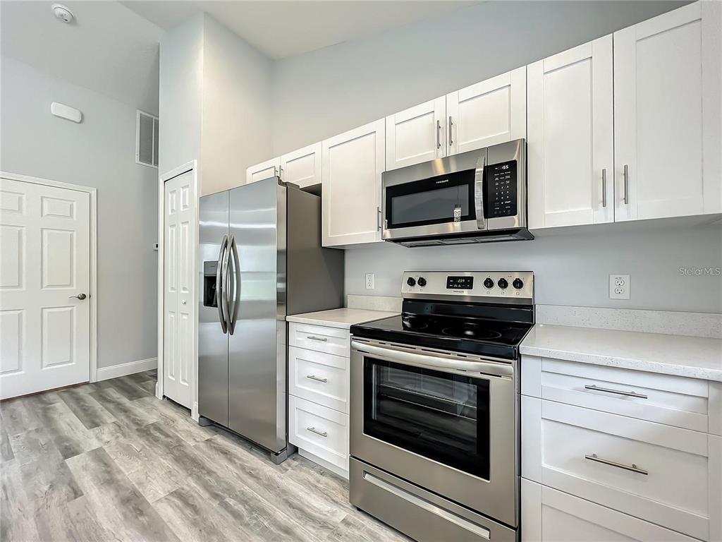 A kitchen features white cabinets, stainless steel appliances, and gray wood-look flooring — 15962 SW 53RD COURT, OCALA, FL