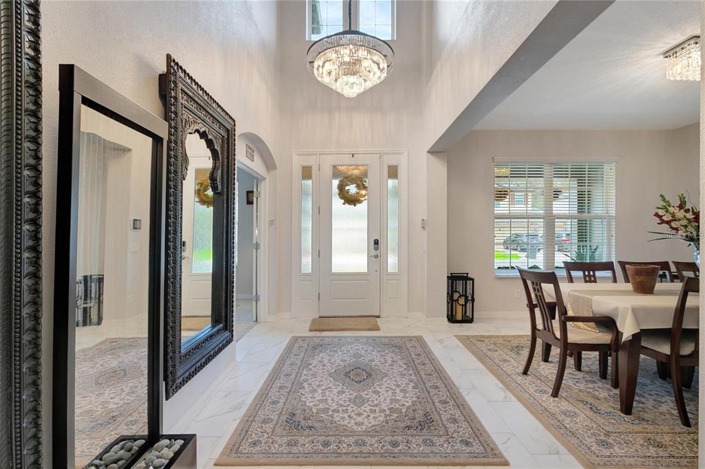A bright entryway features a crystal chandelier, high ceilings, tile flooring, and a dining area — 19335 EAGLE CREEK LANE, TAMPA, FL