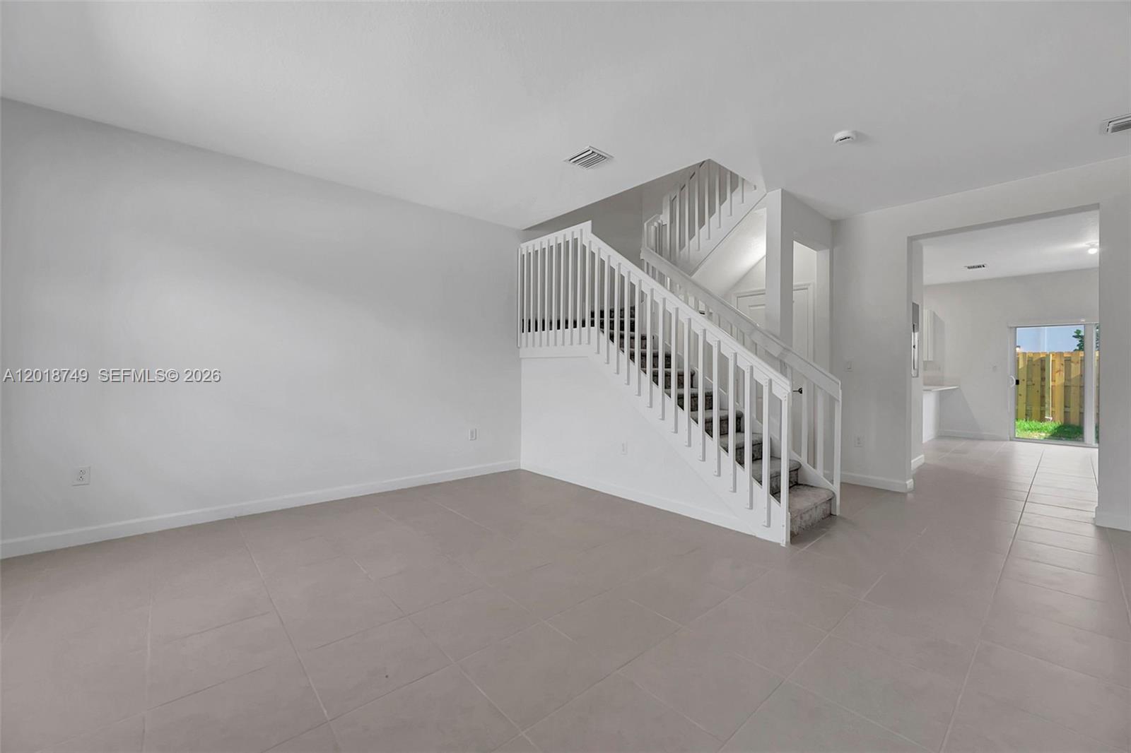 A bright living room features light tile flooring, white walls, and a central staircase — HOMESTEAD, FL