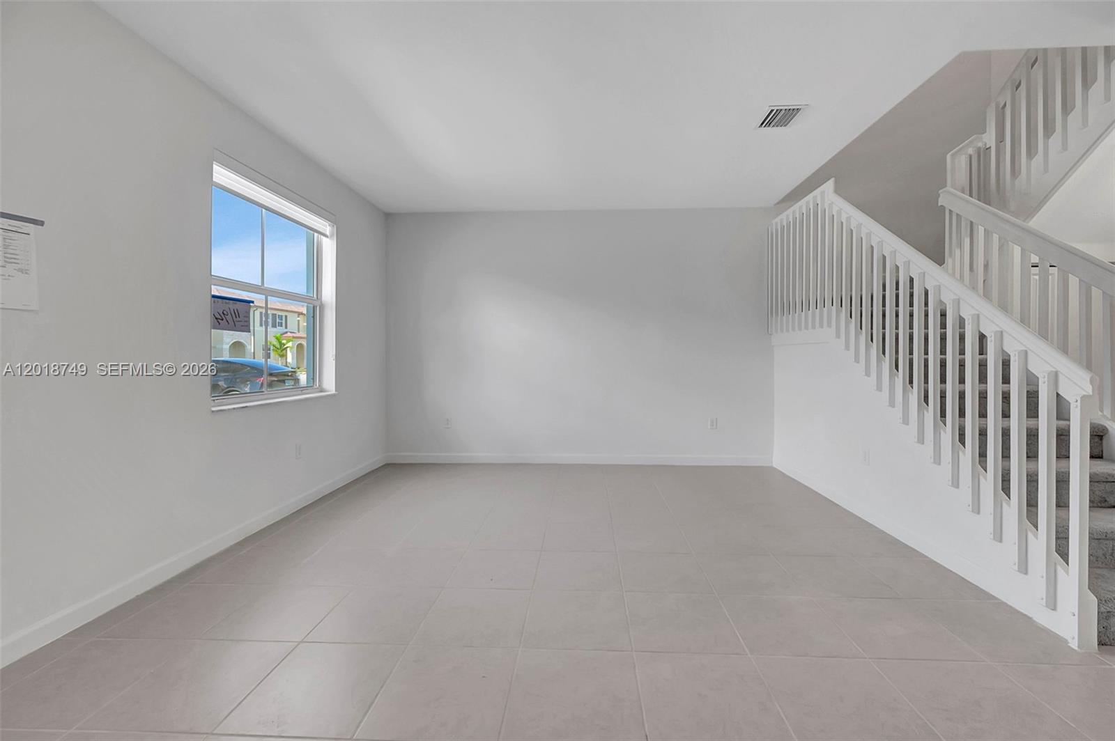 An empty room with light tile flooring, white walls, a window, and a staircase — HOMESTEAD, FL