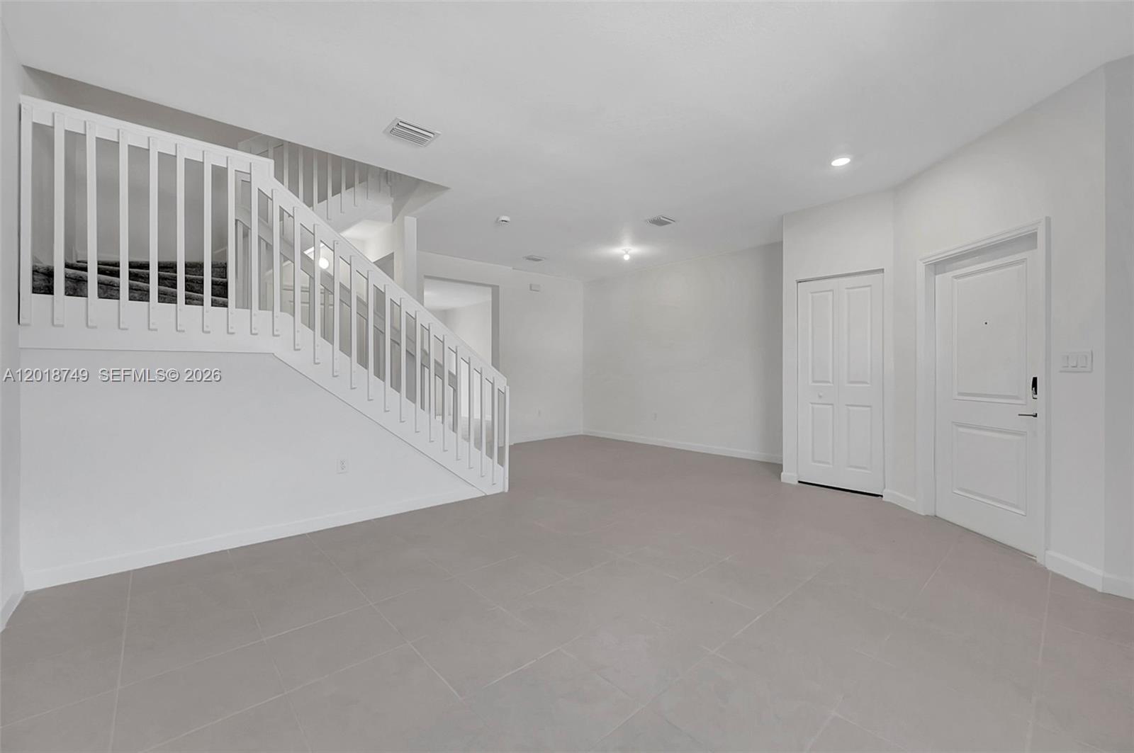 An empty room features white walls, gray tile flooring, a staircase, and two white doors — HOMESTEAD, FL