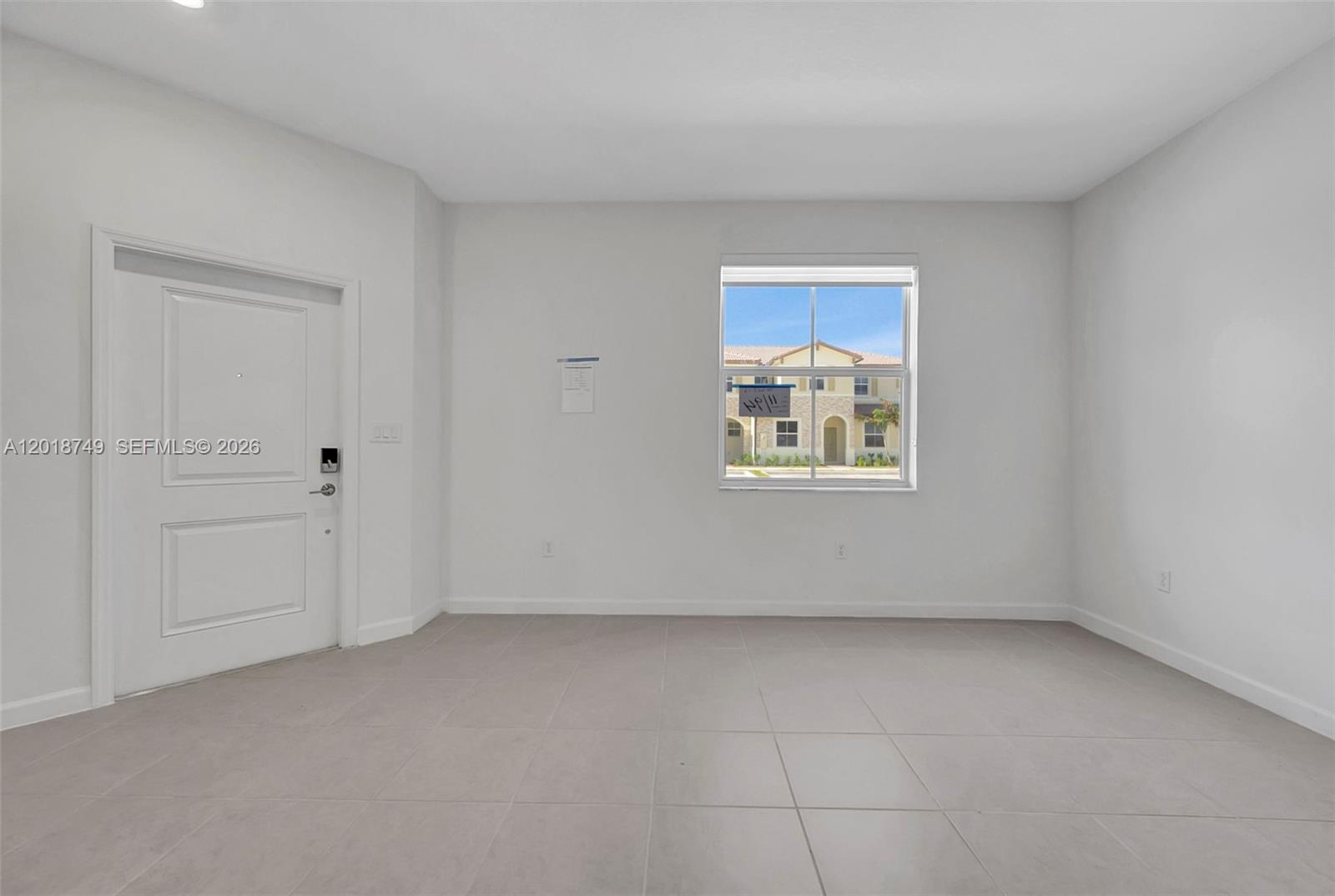 An empty room with white walls, light tile flooring, a white door, and a window — HOMESTEAD, FL