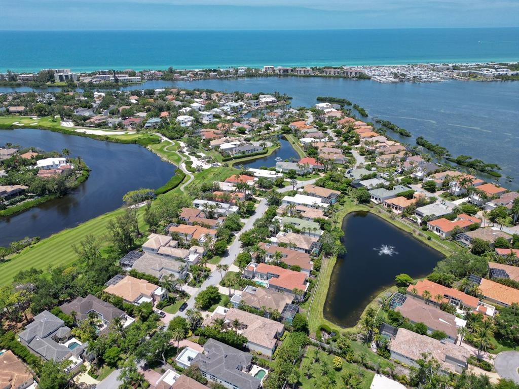 An aerial view shows a residential neighborhood with houses, ponds, and a golf course near water — 3527 FAIR OAKS LANE, LONGBOAT KEY, FL